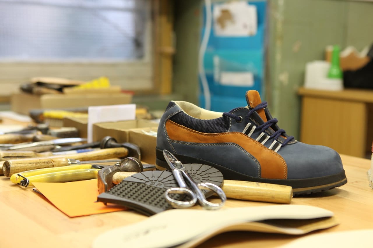 Orthopädischer Maßschuh aus blauem und cognacfarbenem Leder auf der Werkbank, davor Werkzeug